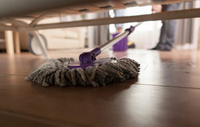 Guy mopping the dust under sofa in apartment.